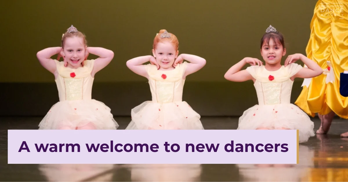 Three girls in pink tutus smiling while sitting on dance studio floor.
